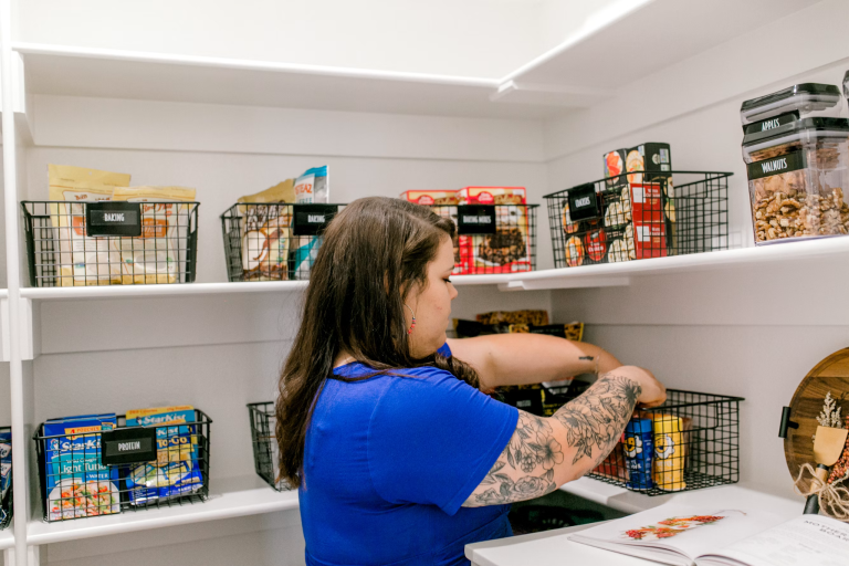 Woman organizing pantry shelves with labeled storage bins as part of thoughtful home management and home organization.
