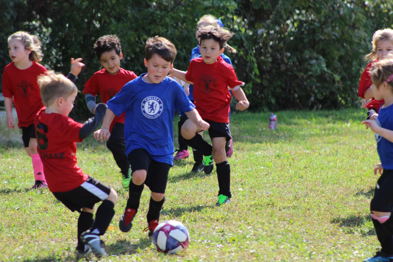 Children playing soccer during a youth sports game while learning teamwork, confidence, and athletic skills.