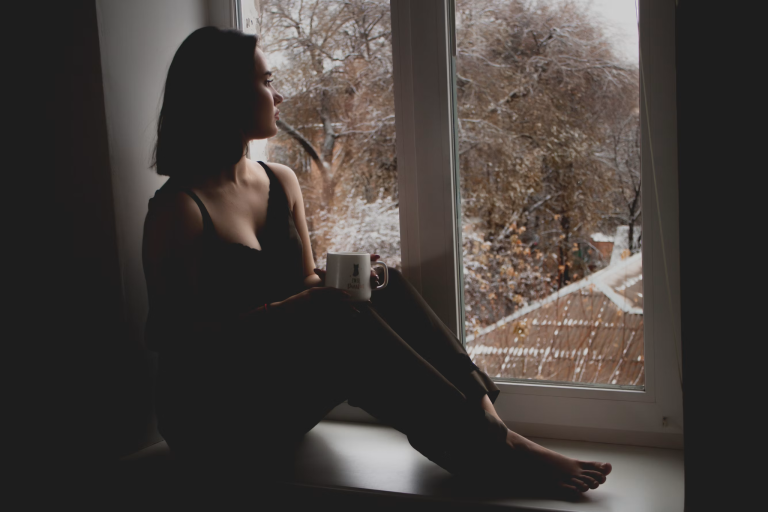 Woman sitting quietly by a window reflecting during emotional recovery after trauma