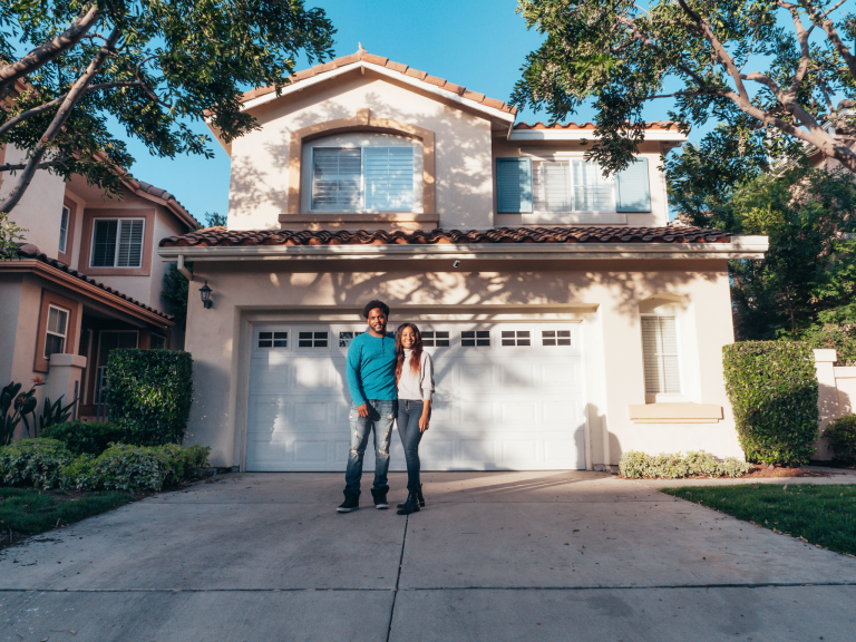 Couple standing in front of their well-maintained home, representing home resilience, preparedness, and long-term homeownership.