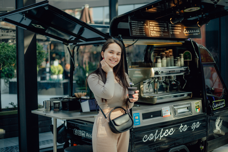 Woman standing in front of a mobile coffee trailer, highlighting a flexible small business built on wheels.