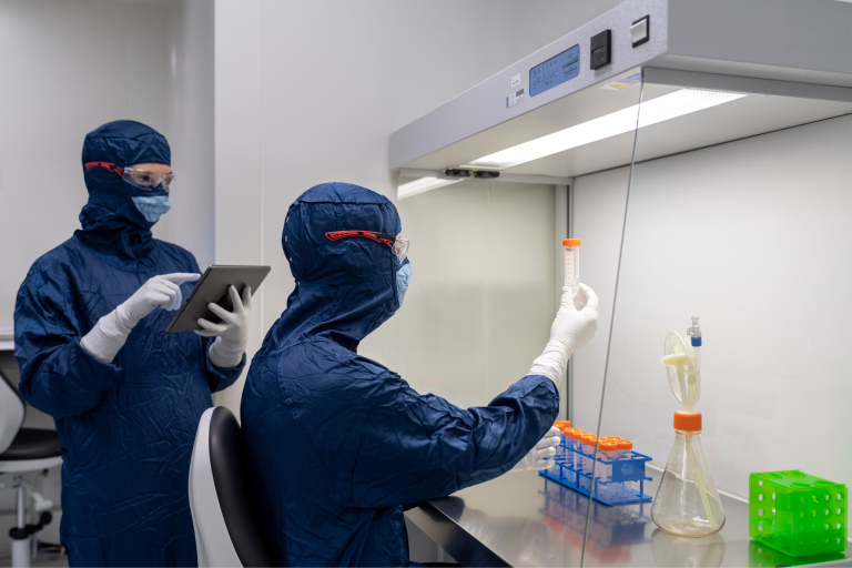 Pharmaceutical technicians wearing protective cleanroom gear use precision equipment to inspect and handle sterile laboratory samples.