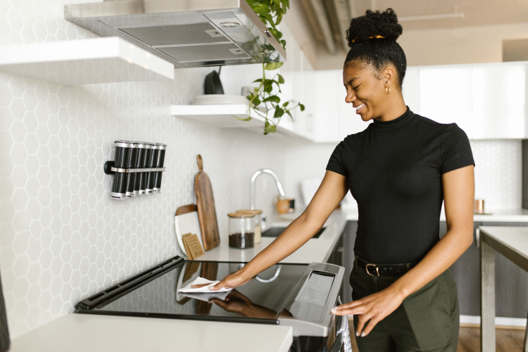 Woman wiping a clean kitchen stovetop during a weekly kitchen cleaning routine.