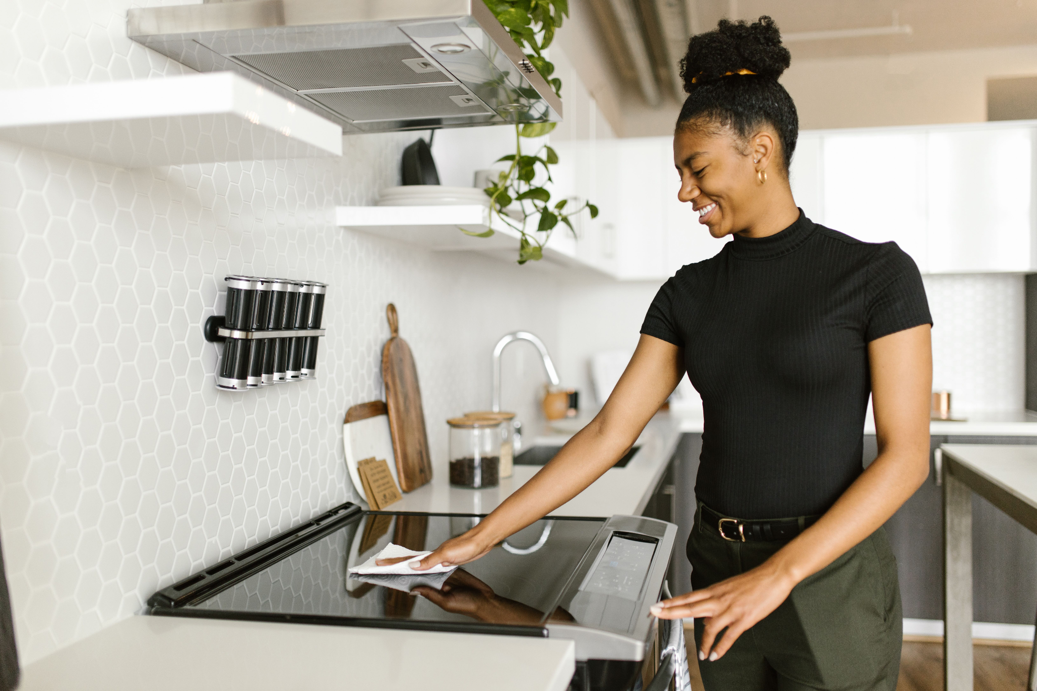 Woman wiping a clean kitchen stovetop during a weekly kitchen cleaning routine.