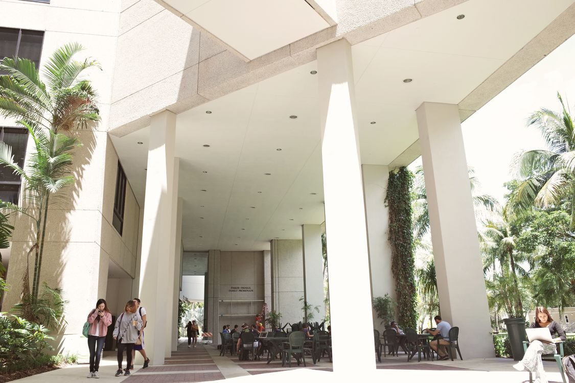 Students walking and studying outside a college campus building on a sunny day.