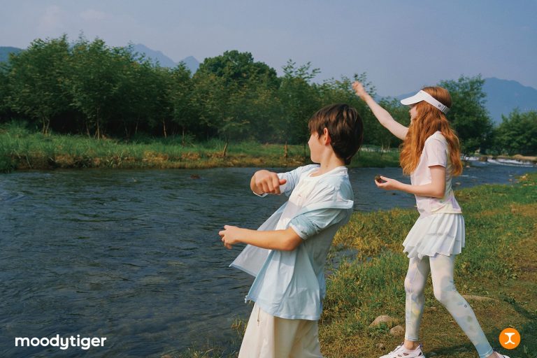 Two children wearing lightweight activewear play by a river, demonstrating comfortable clothing designed for outdoor adventures and active play.