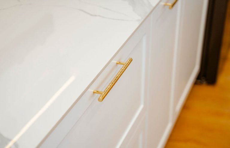 Close-up of white kitchen cabinets with textured gold handles and a white countertop.