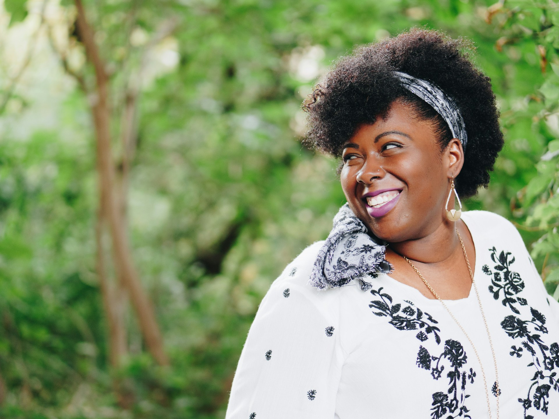 Smiling woman outdoors surrounded by green trees, looking confidently toward the future.