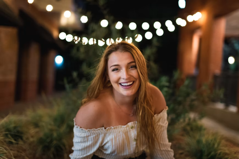 Smiling woman showing a confident, radiant smile in a warmly lit outdoor setting.