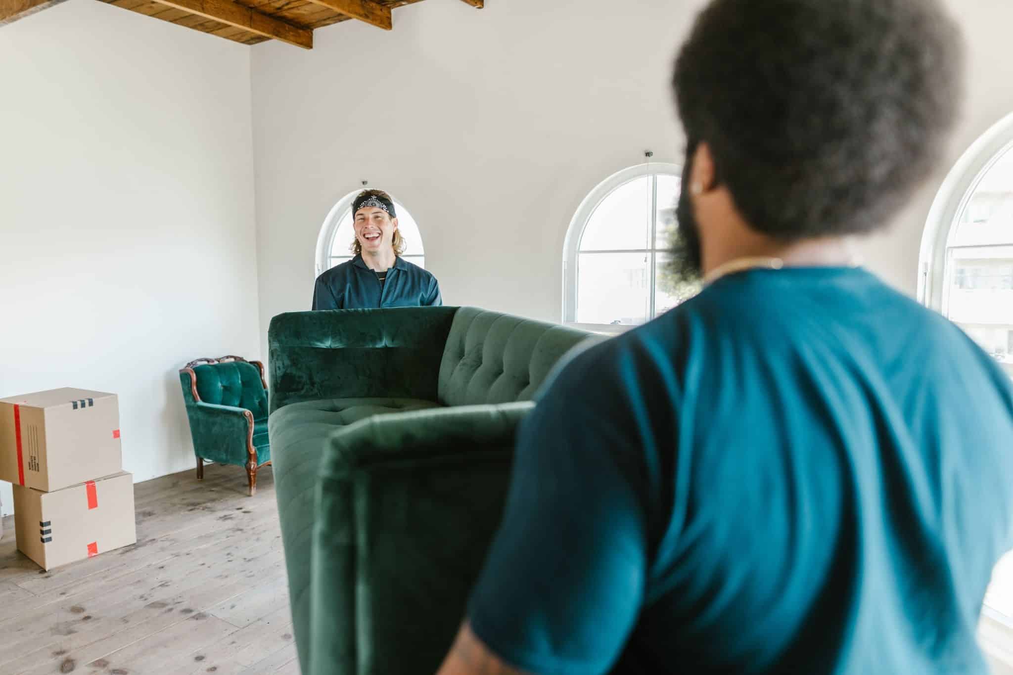 Two movers carry a large sofa into a bright new home during moving day.