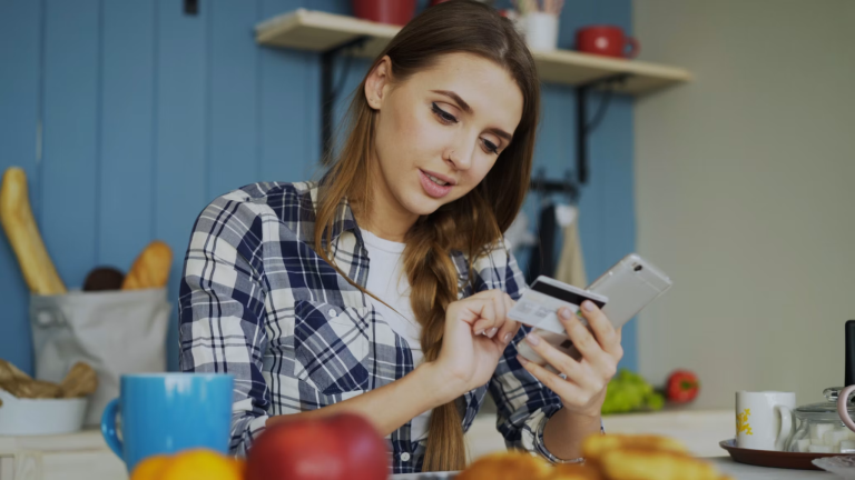 Woman using a smartphone and credit card while managing her finances at home