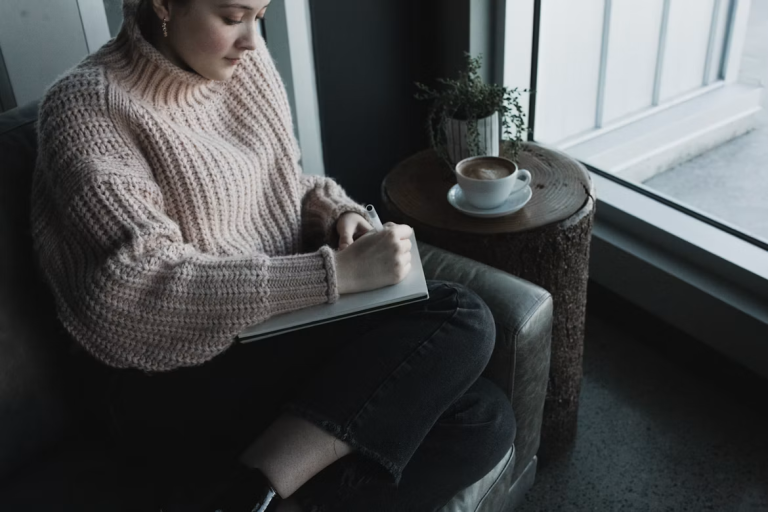 Woman journaling by a window as part of her self-care routine