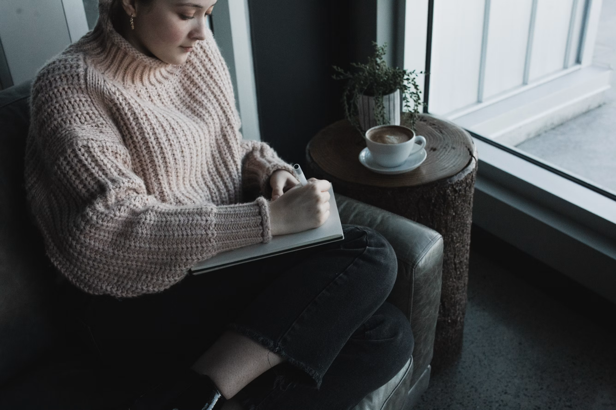 Woman writing in a journal beside a cup of coffee during a quiet moment of spiritual reflection.