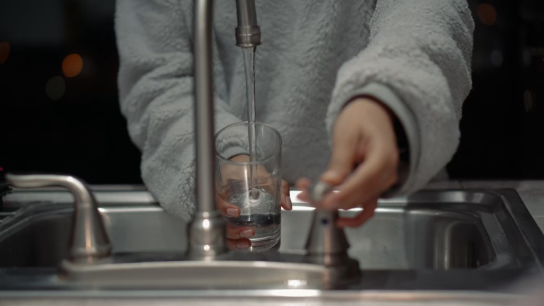 Person filling a glass of water from a kitchen faucet during routine home maintenance