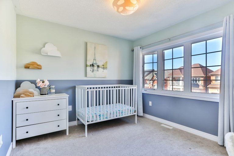 Calm baby nursery with white crib, soft blue walls, natural light, and simple decor