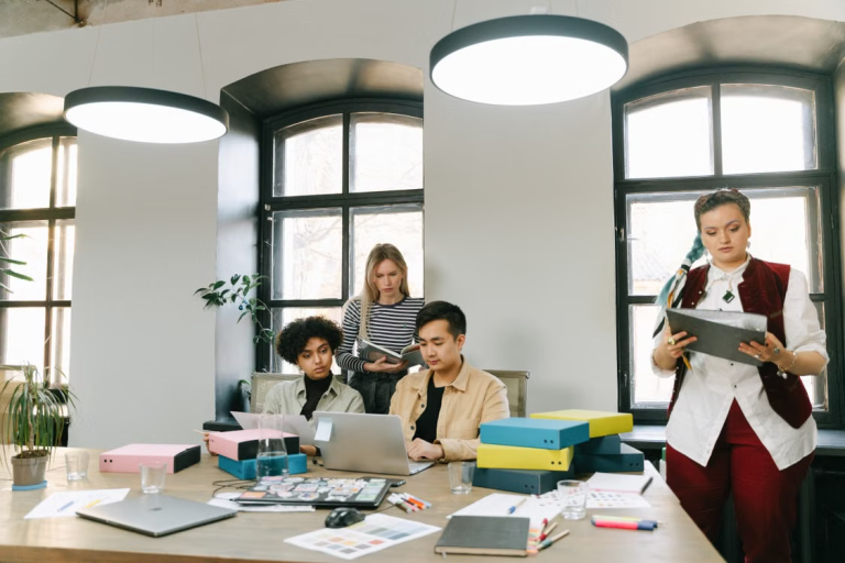 Four coworkers organize folders, laptops, and documents around a large office table.