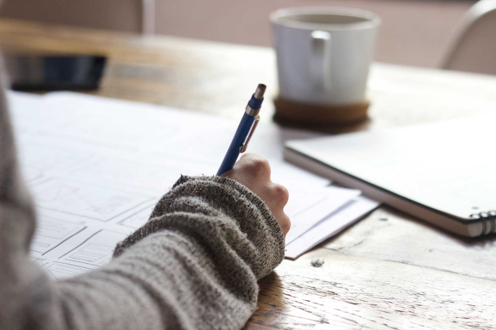 Person completing a written assessment at a desk with a notebook and coffee