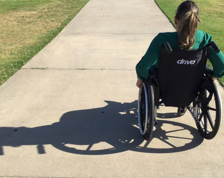 Wheelchair user traveling along a paved path in a public green space.