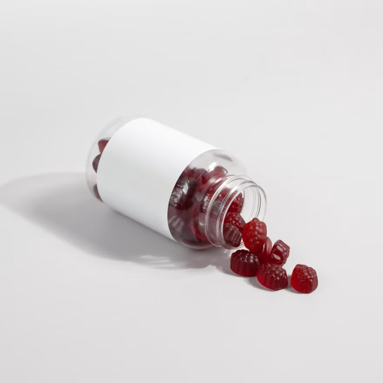 Unlabeled bottle with red gummy edibles spilling onto a white surface.