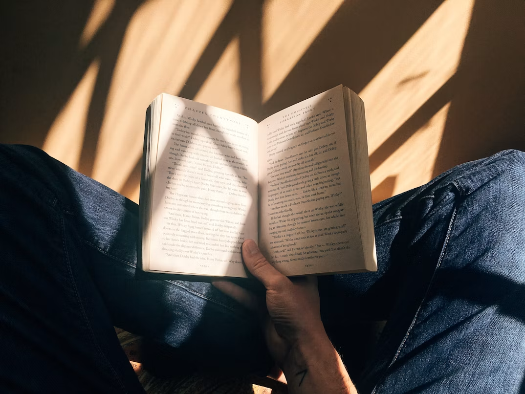Person reading an open book while sitting in warm sunlight.