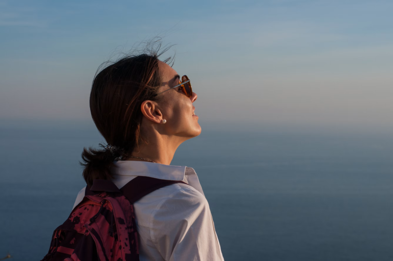 Woman wearing a backpack pauses to reflect while overlooking the ocean during a life transition.