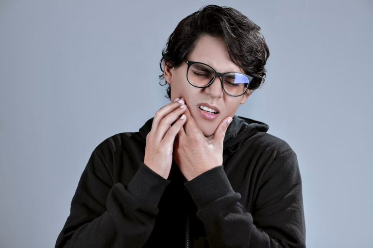 Person wearing glasses holding their jaw with a pained expression.
