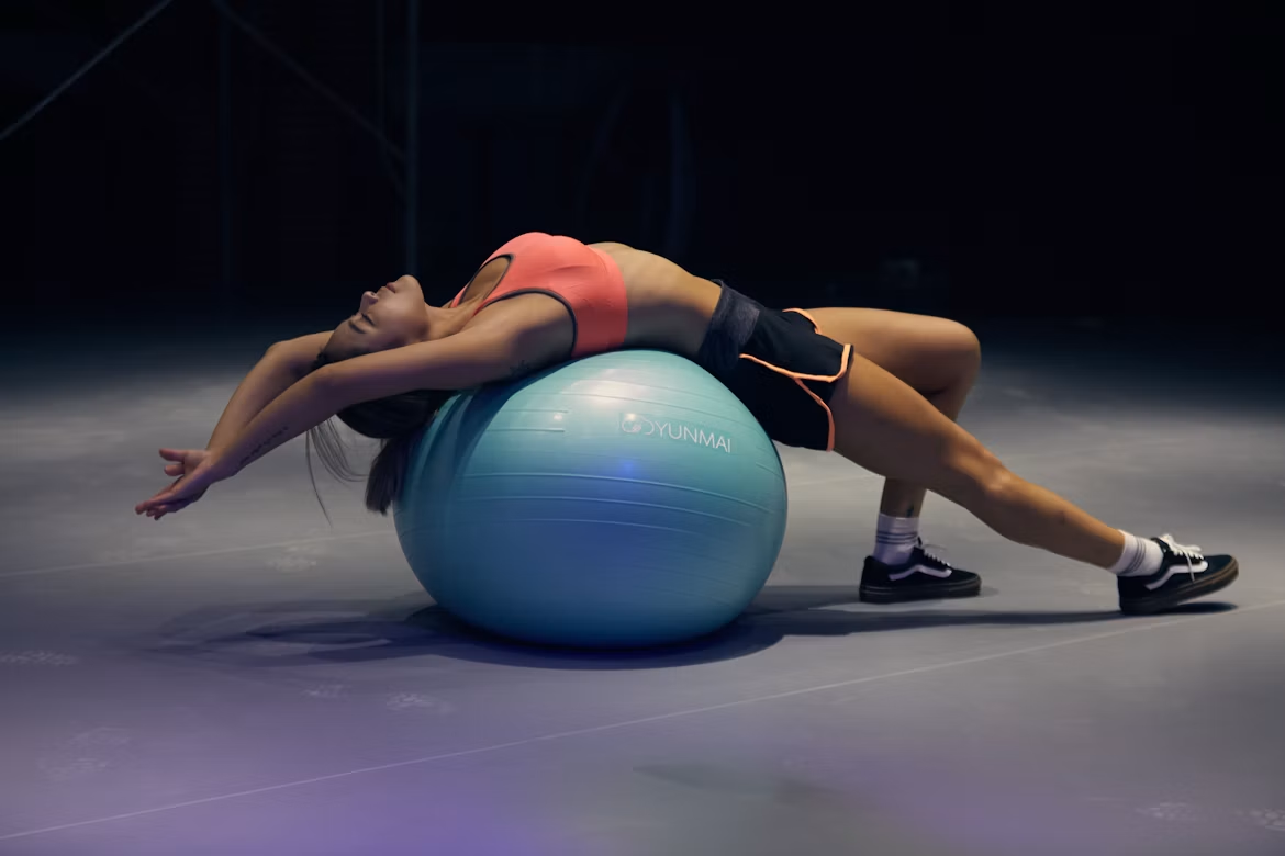 Woman performing a backbend stretch on a stability ball in a fitness studio.