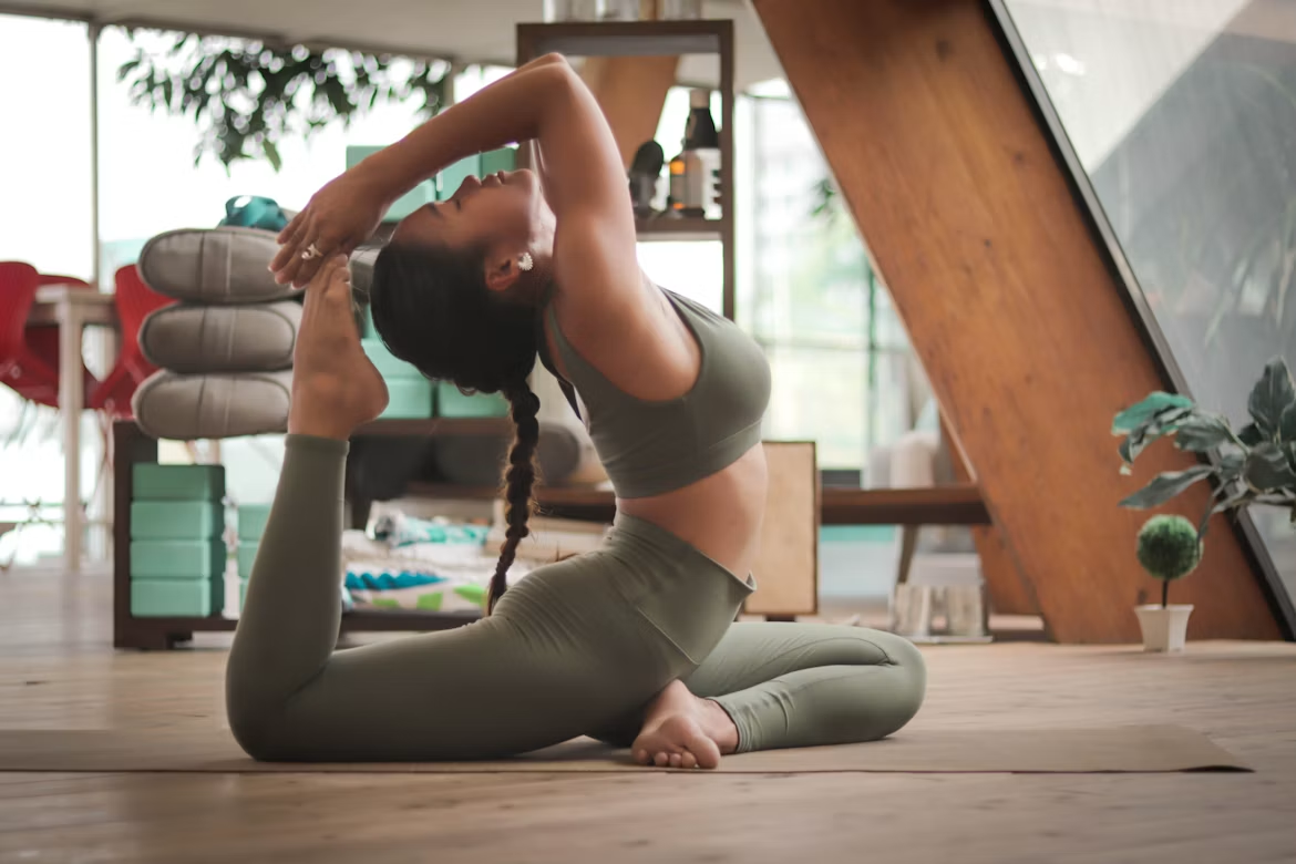 Woman practicing a seated yoga stretch on a mat in a bright indoor studio.