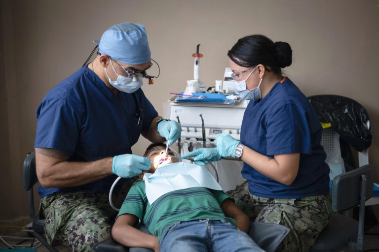 Two dental professionals provide care to a child in a dental chair.