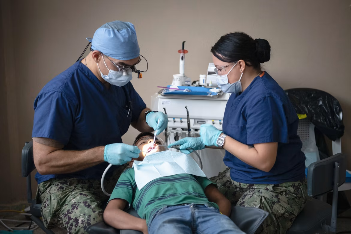 Two dental professionals provide care to a child in a dental chair.