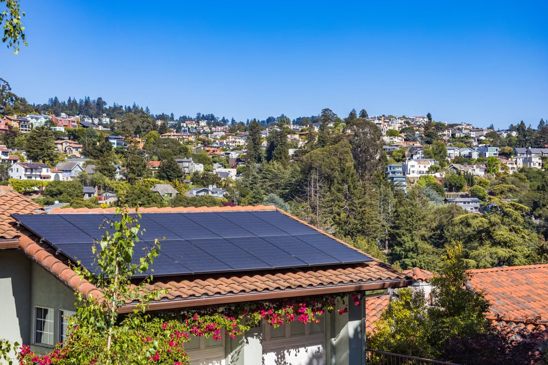 Rooftop solar panels installed on a tiled home in a leafy residential neighborhood.