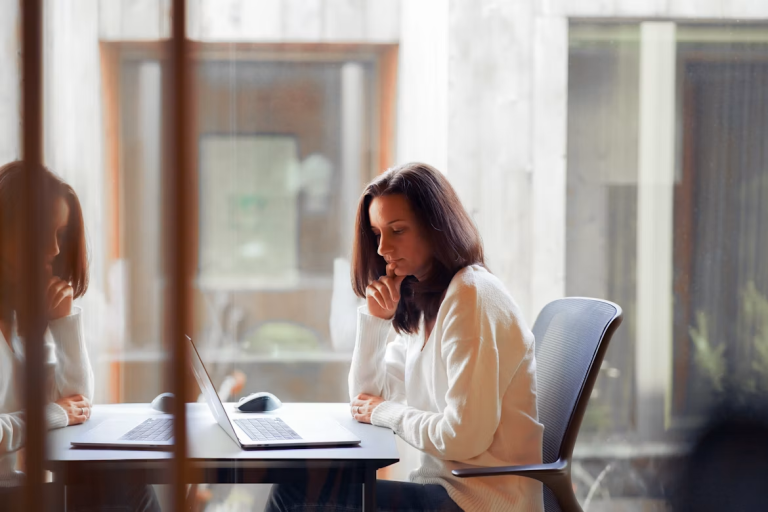 Woman reviewing a laptop at a desk in a bright office.