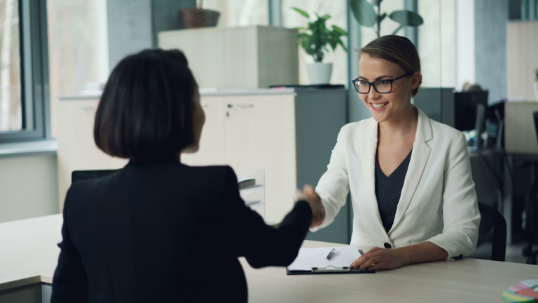 Two professionals shake hands during a positive workplace conversation that reflects trust, respect, and compassionate leadership.