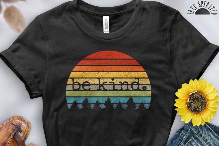 Black graphic T-shirt featuring a colorful retro sunset design with the words “be kind”