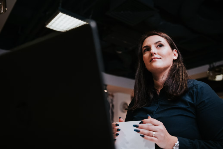 Woman holding a notebook while looking thoughtfully upward in a professional workspace.