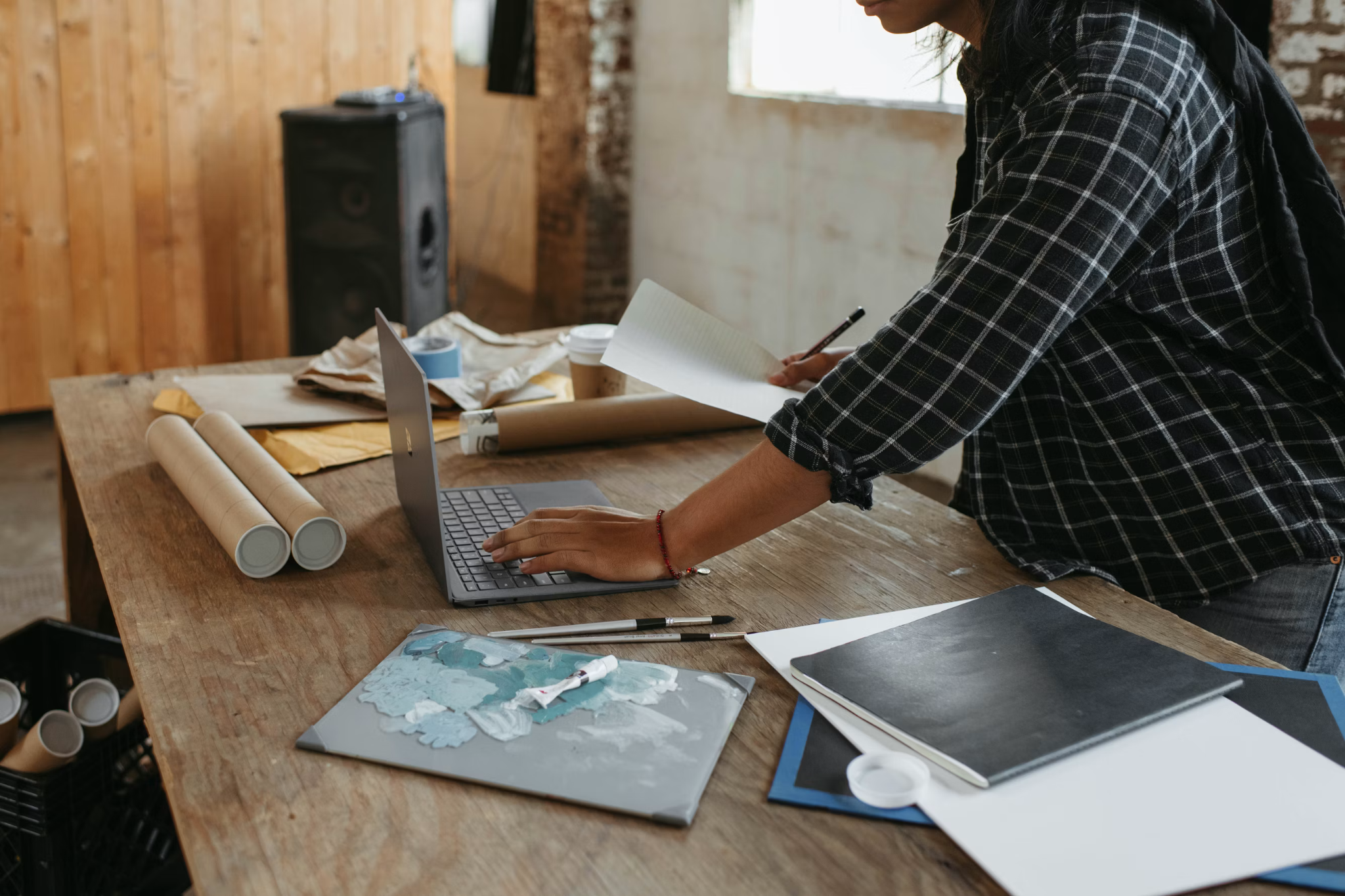 Person sketching ideas and using a laptop while planning a creative project at a worktable.