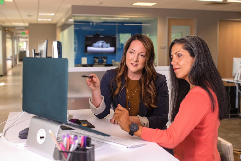 Two women review information together on a desktop computer in an office.