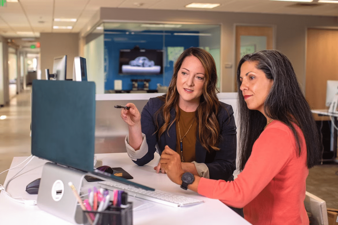 Two women review information together on a desktop computer in an office.
