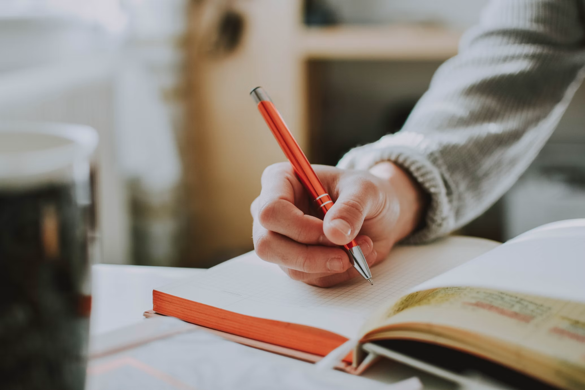 Close-up of a person writing in an open notebook with a red pen