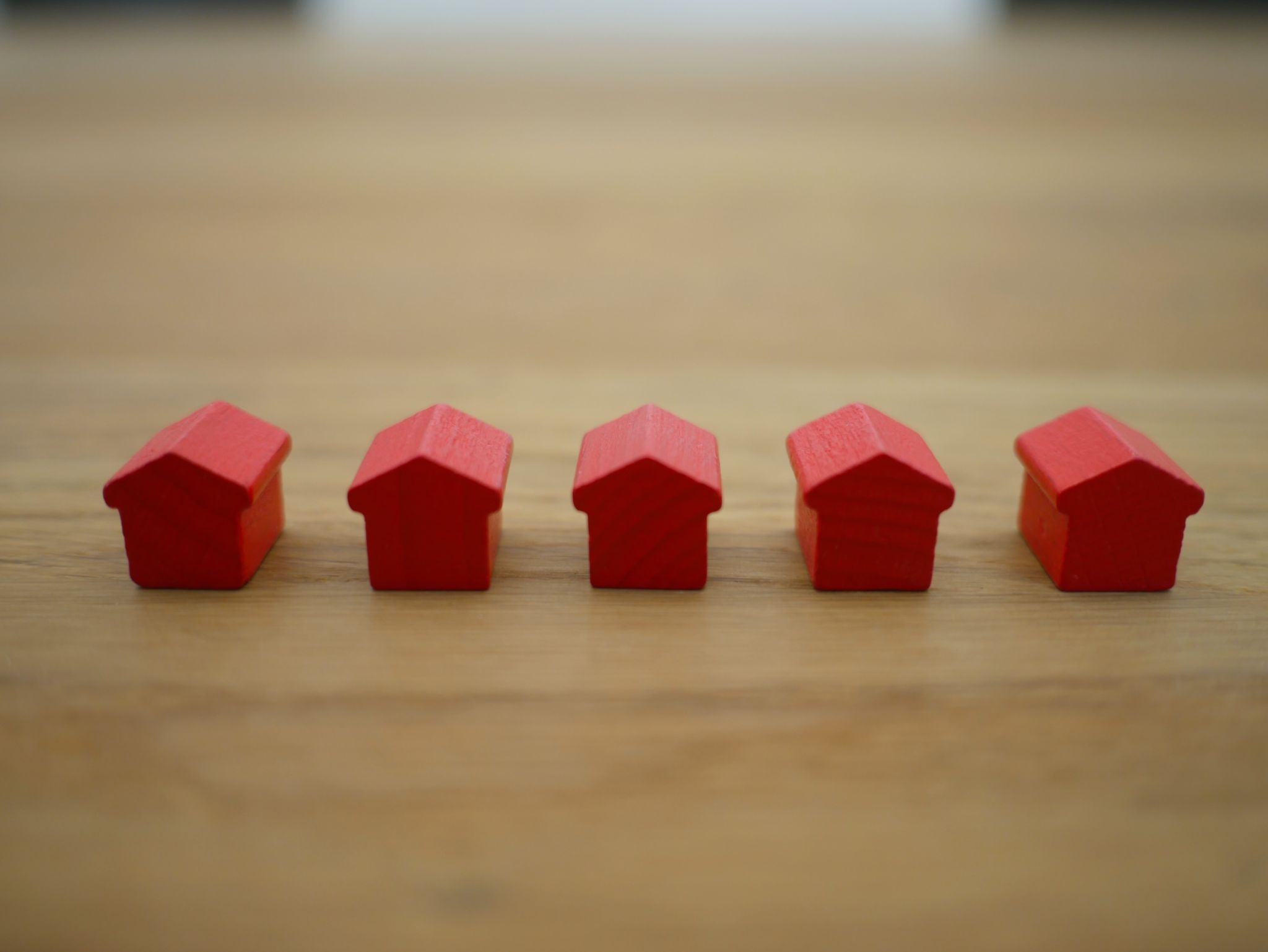Five small red wooden house figures arranged in a row on a wooden surface