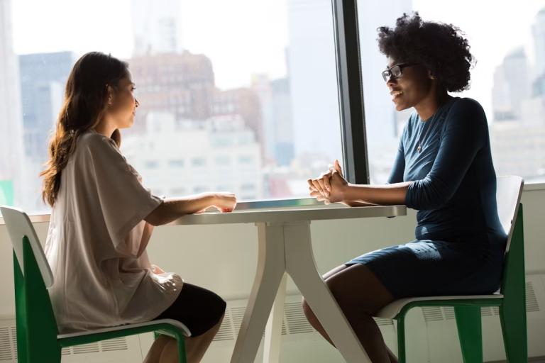 Two women having a focused conversation across a table near a large window