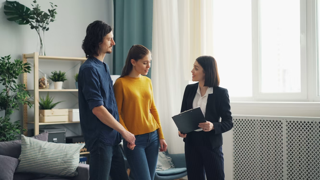 Property manager speaking with a couple in a bright apartment while holding a clipboard.