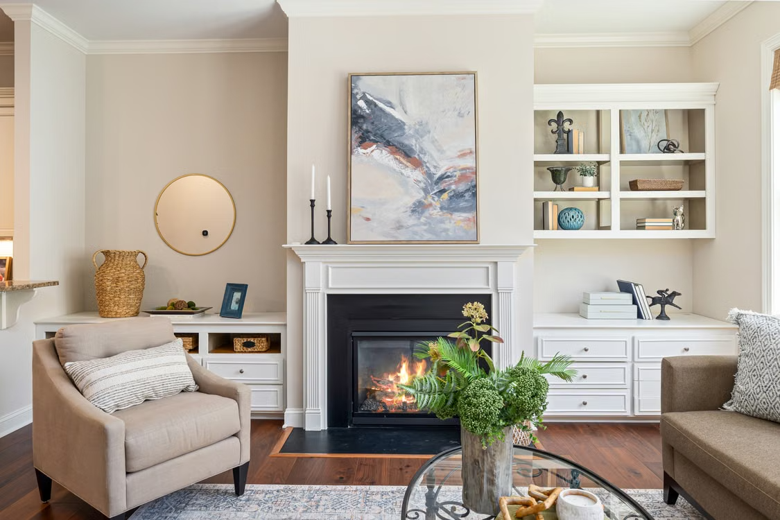 Neutral living room with a fireplace, built-in shelves, armchairs, and a glass coffee table
