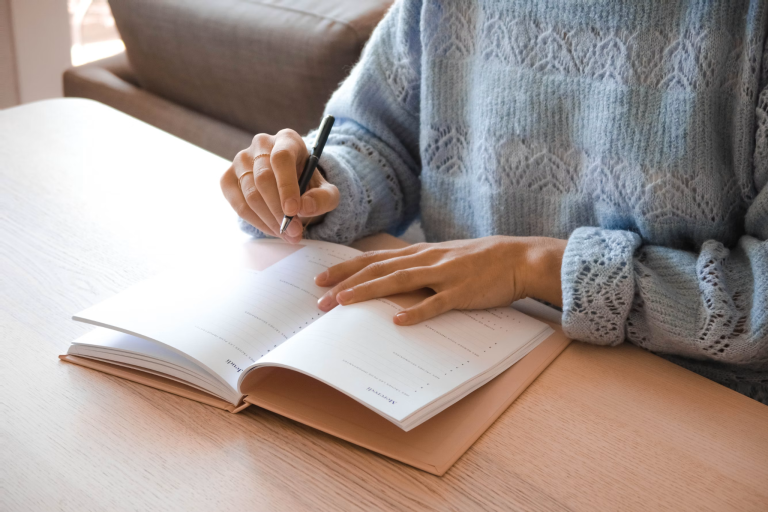 Person writing in an open planner at a wooden table