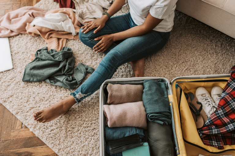 Traveler sitting beside an open suitcase packed with folded clothes and shoes
