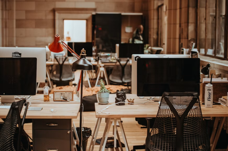 Open office workspace with desks, computer monitors, chairs, and desk lamps