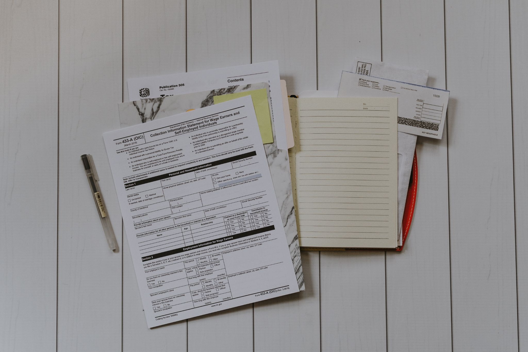 Tax forms, receipts, notebook, pen, and paperwork arranged on a white table