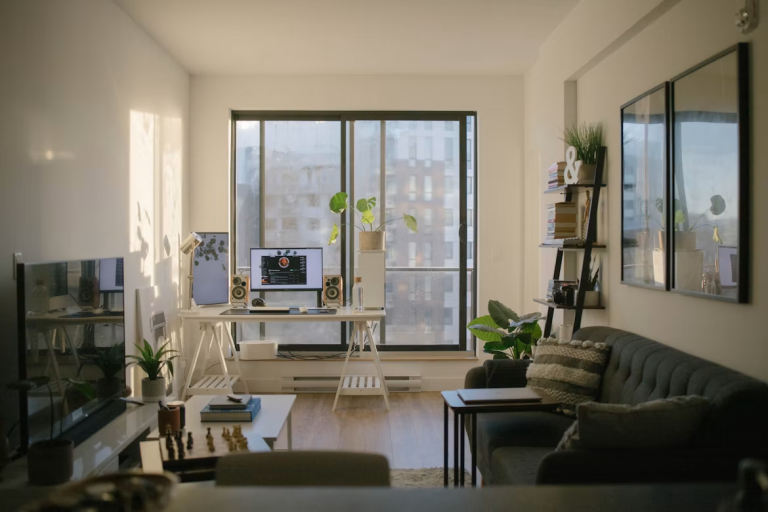 Bright living room with a desk workspace, computer, plants, and sofa near large windows