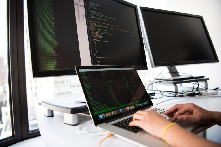 Person working on a laptop connected to monitors displaying software code
