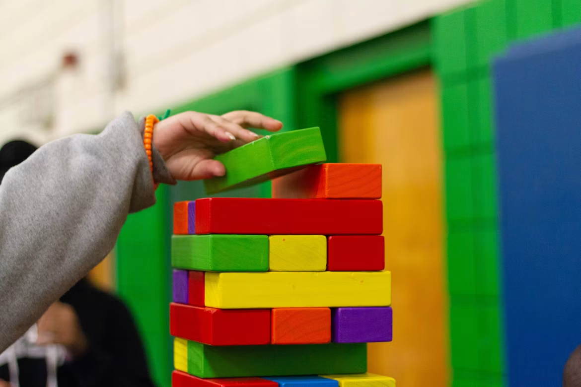 Hand placing a green wooden block on a tower of colorful blocks